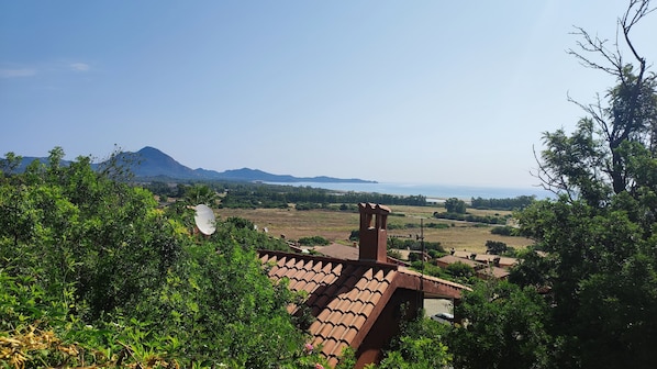 A traditional building with a tiled roof, surrounded by lush greenery and a view of distant mountains and a body of water.