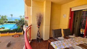 Un balcón con vista a la piscina, una mesa de comedor dispuesta con platos y vasos, y un jarrón decorativo.
