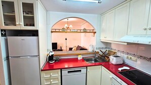 Una cocina compacta con armarios blancos, una encimera roja y un lavavajillas integrado.