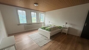 Un dormitorio con piso de madera, una cama con ropa de cama verde, una mesita de noche y un radiador debajo de una ventana.