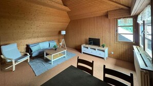 Una habitación acogedora con techo de madera, un sofá, una mesa de centro, un televisor sobre un mueble blanco y una ventana con vistas.
