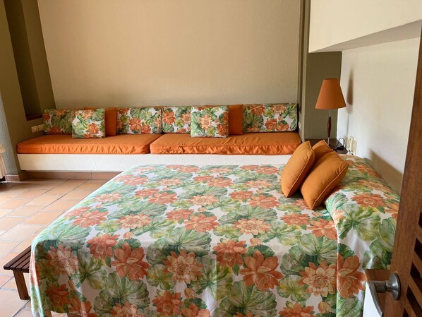 A bedroom with a bed, a sofa bed with floral cushions, a bedside table, and a lamp. - Yeguas W37 by Wynwood House (Anapoima)