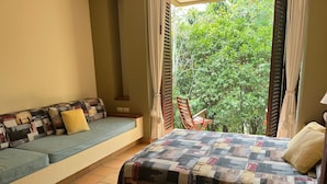 A bedroom with a bed, a sofa, and a window with a view of greenery. - Yeguas W37 by Wynwood House (Anapoima)