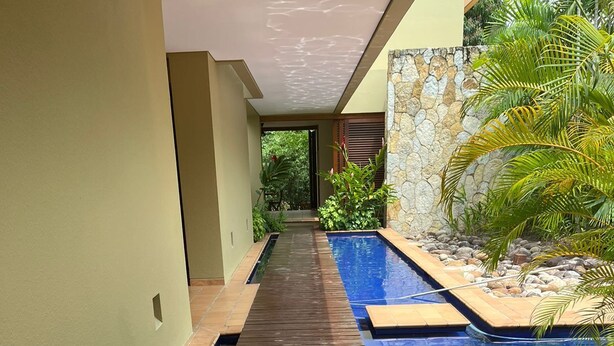A wooden deck leading to a swimming pool with a stone wall and tropical plants. - Yeguas W37 by Wynwood House (Anapoima)