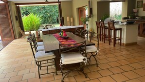 A spacious dining area with a long table, multiple chairs, and a kitchen area visible in the background. - Yeguas W37 by Wynwood House (Anapoima)