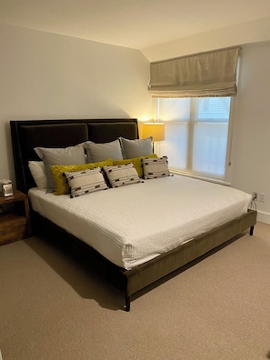 A bedroom with a large bed, a bedside table, a lamp, and a window with a view.