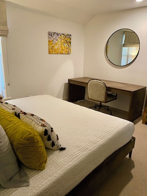 A bedroom with a bed, a desk, a chair, a round mirror, and a wall art piece.