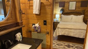 Een houten interieur met een badkamer en een slaapkamer, inclusief een wastafel, handdoekhouder en een bed met kussens.