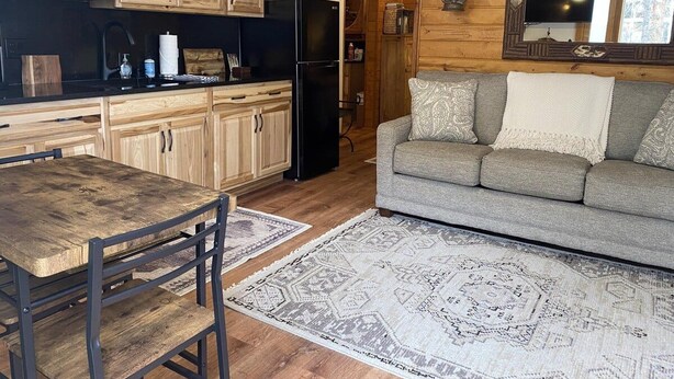 Een keuken met houten kastjes, een zwarte koelkast en een eettafel met stoelen.