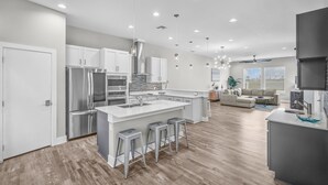 A modern kitchen with a large island, stainless steel appliances, and a dining area with a sofa and coffee table. - Waterfront Condo With Rooftop + Pool + Boat Slips (Corpus Christi)