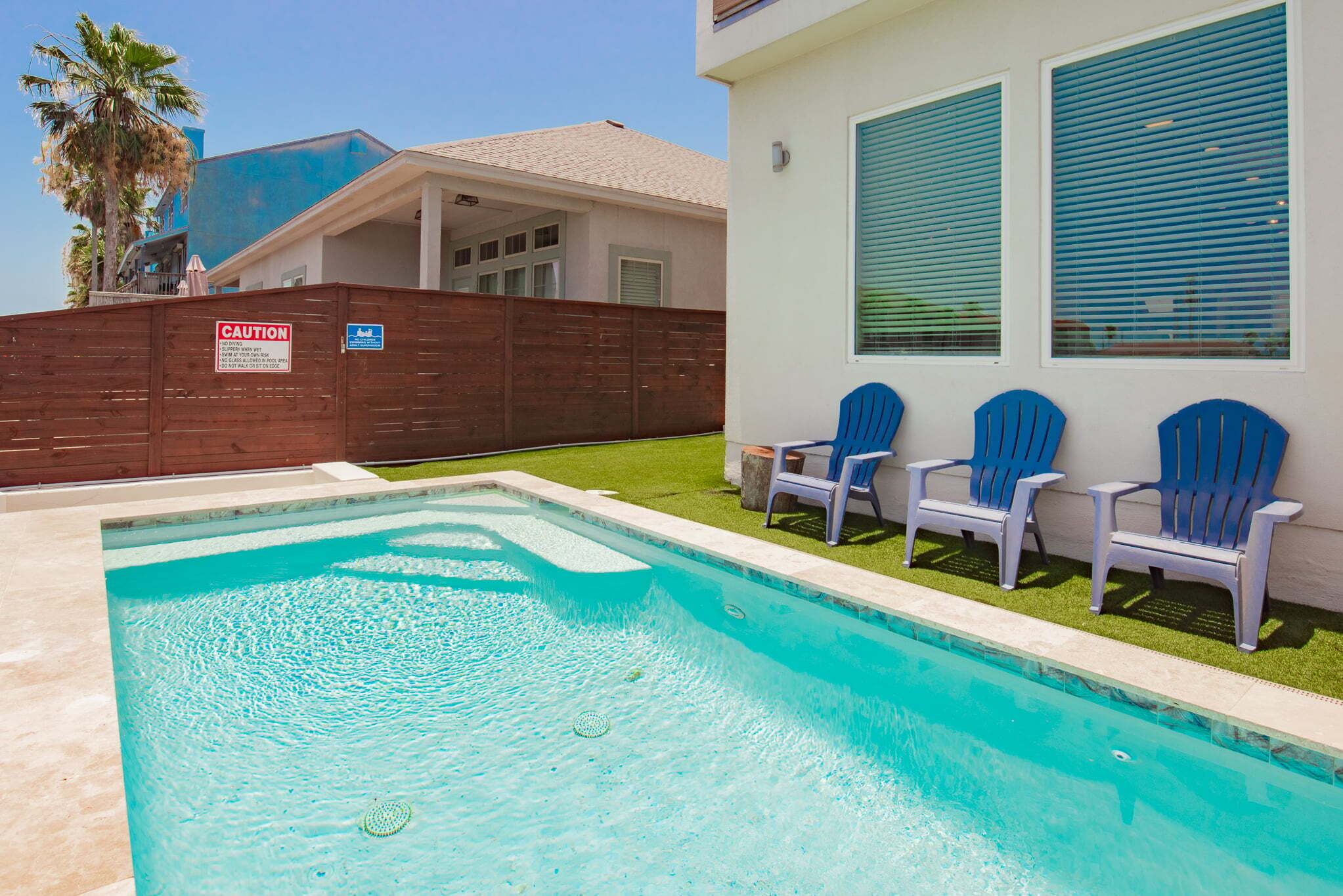 A swimming pool with a wooden fence, blue chairs, and a building with windows.