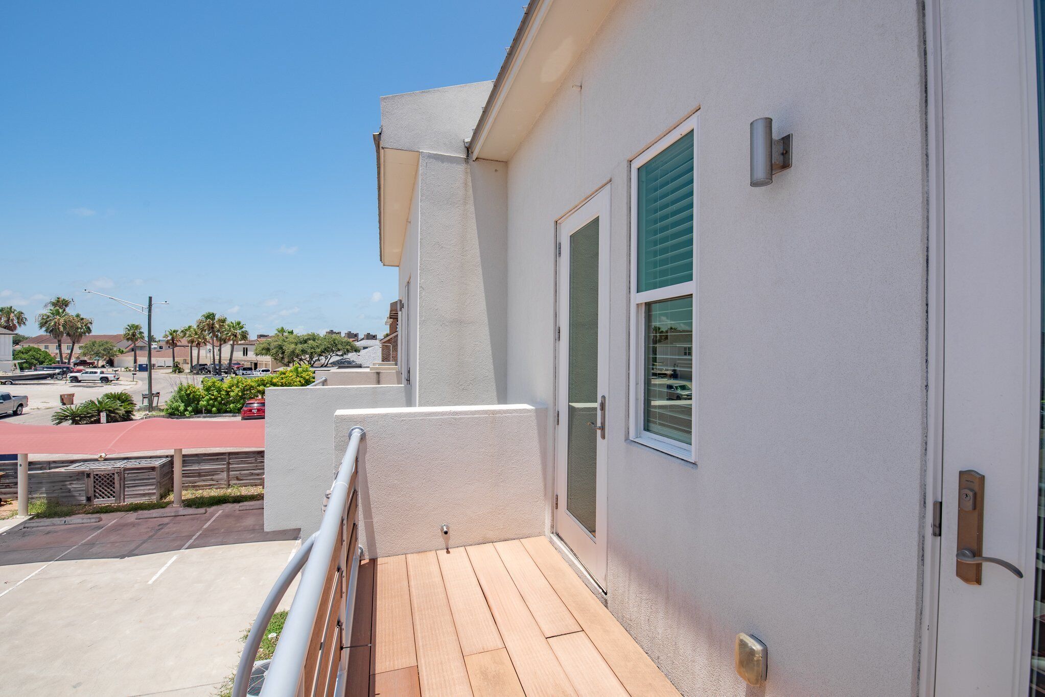 Un balcon doté d’un plancher en bois, d’un mur extérieur blanc et d’une porte-fenêtre coulissante avec un store vert.