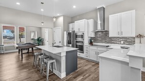 A modern kitchen with white cabinets, a central island, and a dining area with a pool table. - Waterfront Condo With Rooftop + Pool + Boat Slips (Corpus Christi)