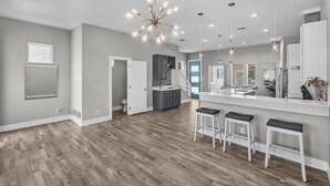 A spacious kitchen with a central island, a dining area with bar stools, and a modern chandelier. - Waterfront Condo With Rooftop + Pool + Boat Slips (Corpus Christi)