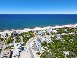 An aerial view of a coastal residential area with houses, a beach, and a clear blue sky. - Little Sunshine (Cape San Blas)