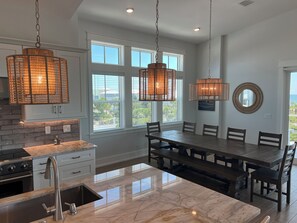 A modern kitchen with a marble countertop, stainless steel appliances, and a dining area with a large table and chairs. - Little Sunshine (Cape San Blas)