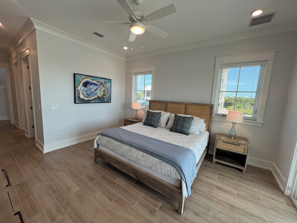 A bedroom with a large bed, two bedside tables with lamps, a ceiling fan, and a window with blinds.
