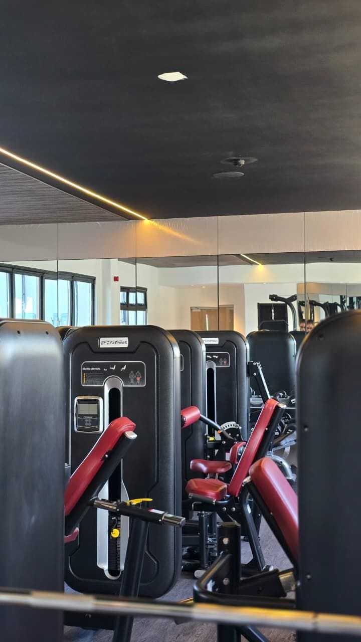 A gym with exercise machines, a ceiling fan, and large windows.