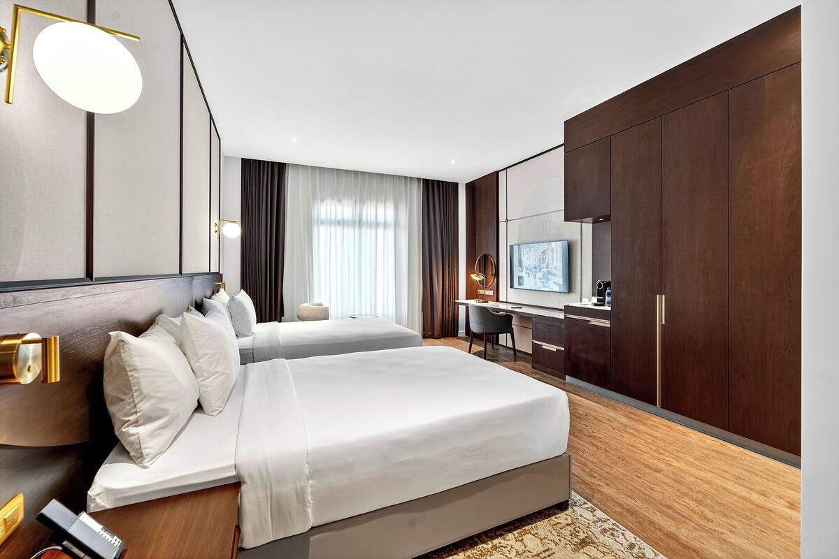 Une chambre d’hôtel moderne équipée de deux lits, d’un bureau, d’une télévision et d’une grande armoire.