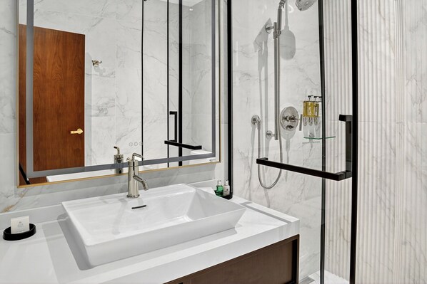 A modern bathroom with a large white sink, a mirror, and a glass-enclosed shower area.