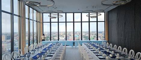 A conference room with a long table set for a meeting, large windows offering a city view, and modern circular ceiling lights.