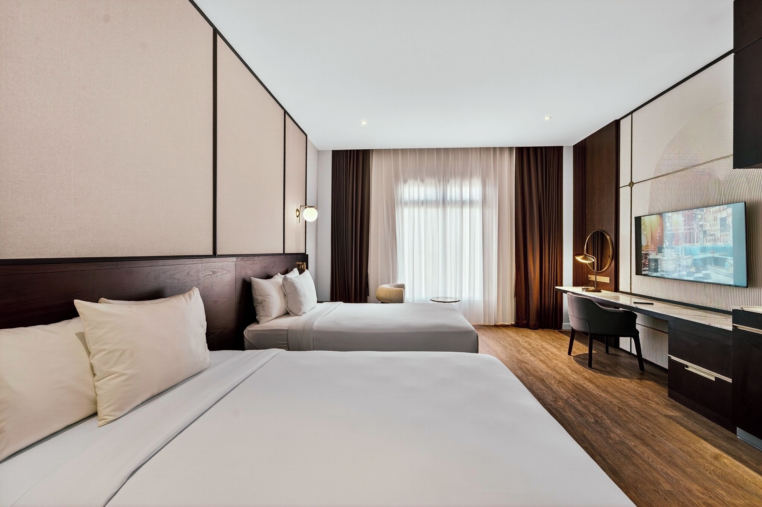 Une chambre d’hôtel avec deux lits, un bureau, une chaise, une télévision et une grande fenêtre avec des rideaux.