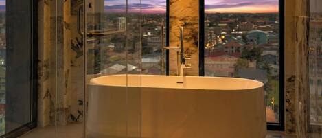 A modern bathroom with a freestanding bathtub, large windows, and a city view.