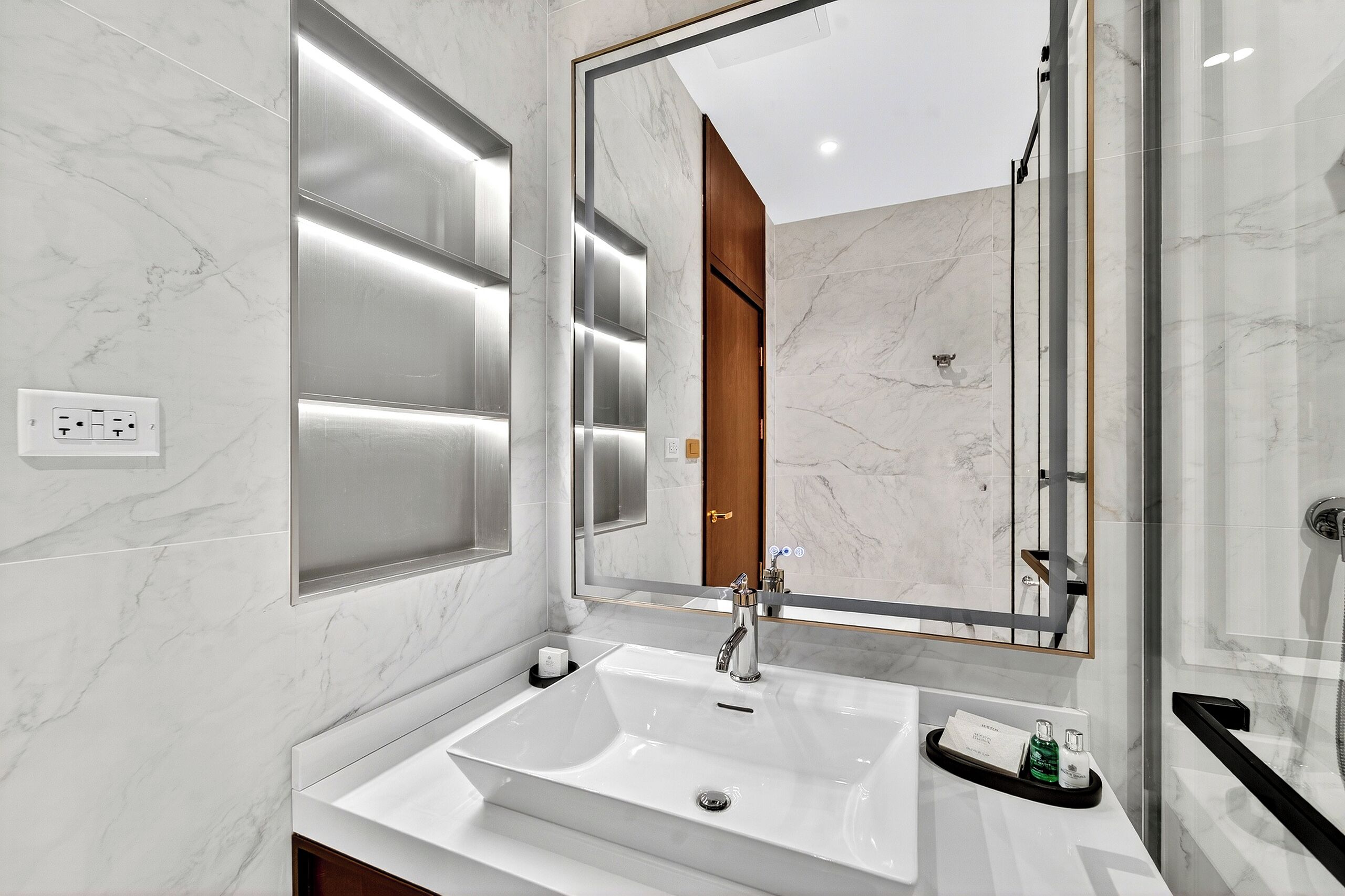 Une salle de bain moderne avec un grand miroir, un lavabo blanc et une douche à parois de verre.