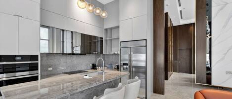 A modern kitchen with a marble island, stainless steel appliances, and a bar seating area.