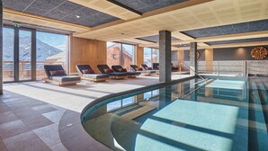 Une piscine intérieure moderne, dotée de chaises longues et offrant une vue sur les montagnes.