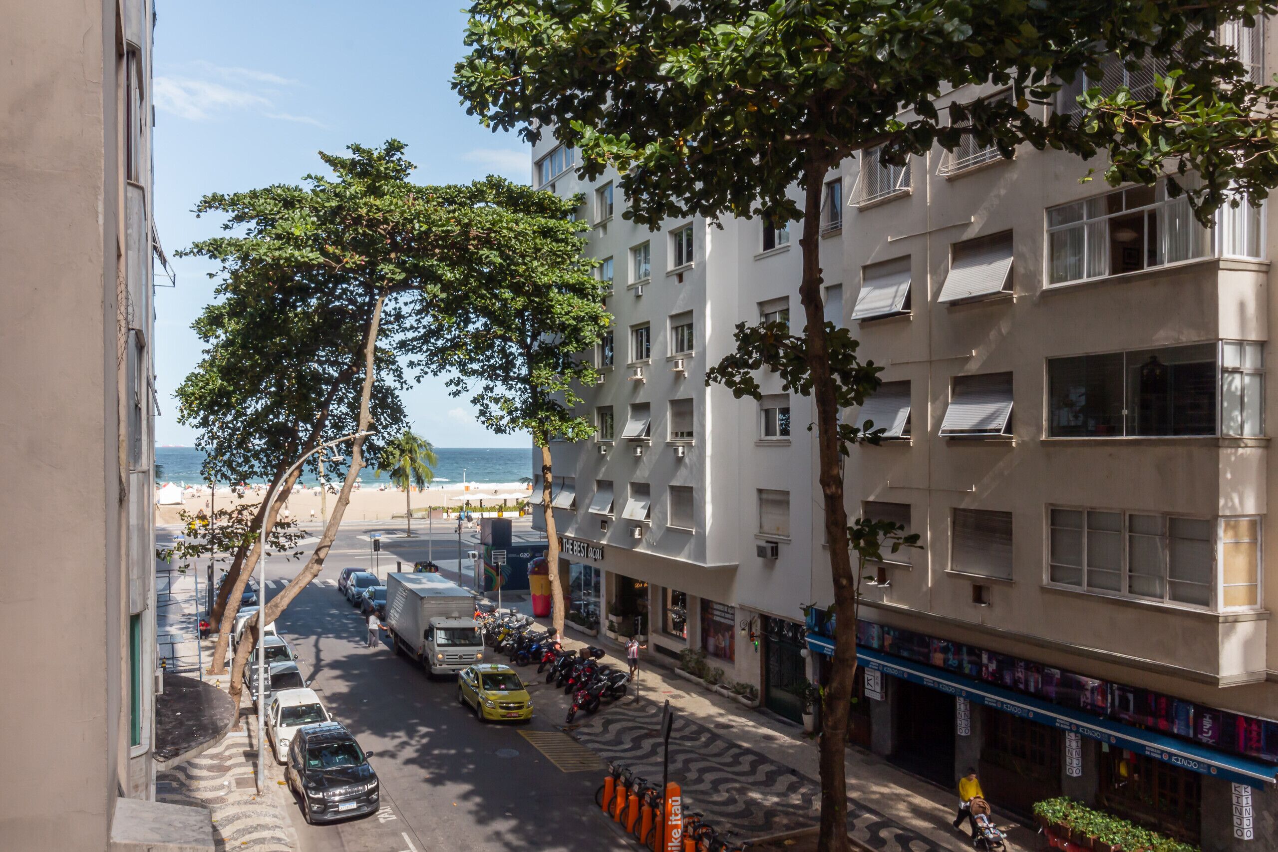 A multi-story building with a beach view, parked cars, and a street with trees.