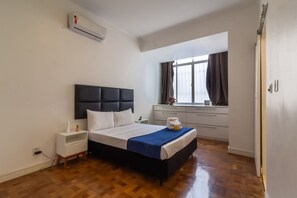 A modern bedroom with a large bed, a bedside table, a nightstand, a window with curtains, and an air conditioning unit. - 2 Minutes From Copacabana Beach D302 (Rio de Janeiro)