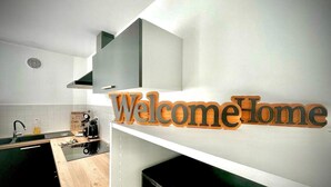 A modern kitchen with a 'Welcome Home' sign, a sink, a coffee maker, and a stove.