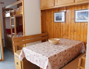 A bunk bed room with a wooden table and chairs, a wooden cabinet, and two framed pictures on the wall.