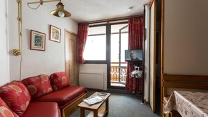 Ein gemütliches Zimmer mit einem roten Sofa, einem Holztisch, einem Fernseher und einem Balkon mit roten Vorhängen.