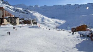 Ein mit Schnee bedeckter Skipistenhang mit Gebäuden und einem Berg im Hintergrund.