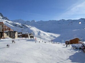 Een met sneeuw bedekte piste voor skiërs, met gebouwen en een berg op de achtergrond.