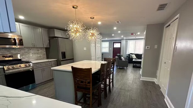 A modern kitchen with a marble countertop, stainless steel appliances, and a dining area with wooden chairs. - Kingdom luxury (Darby)