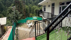 Un balcón con vistas a una cadena montañosa boscosa, un pequeño espacio de estar al aire libre y una escalera que lleva a un nivel superior.