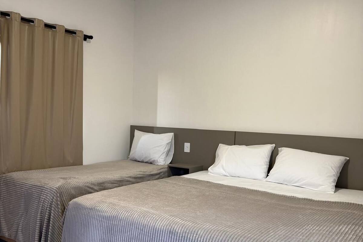 A hotel room with two single beds, beige curtains, and a neutral color scheme.