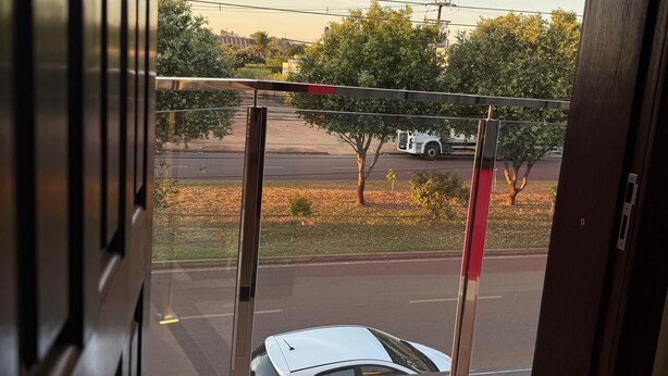 A view from a window with a metal gate and a white car parked outside. - Hotel Jatobás Sinop (Sinop)
