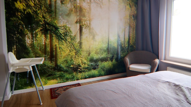 A bedroom with a large forest mural, a bed, a chair, and a window with curtains. - Apartment Braunlage Near Wurmberg Ski Area (Braunlage)