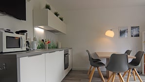 A modern kitchen with white cabinets, a microwave, and a stove. There is a dining table with chairs and a lamp. - Apartment Braunlage Near Wurmberg Ski Area (Braunlage)