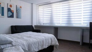 A hotel room with a bed, a desk, and a window with blinds.