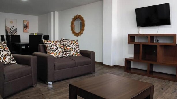 A modern living room with a brown sofa set, a coffee table, a TV mounted on the wall, and a wooden entertainment unit.