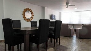 A dining area with a dark wooden table and chairs, a round mirror on the wall, and a television mounted above a sofa.