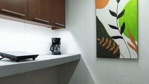 A kitchen with a coffee maker on a counter, a modern cabinet, and a wall-mounted painting.
