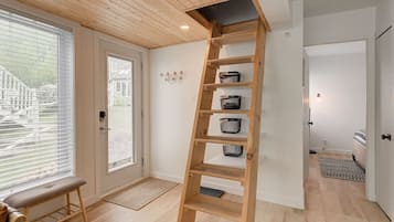 Une étagère en bois avec des paniers de rangement, adossée à un mur blanc, un banc et une porte donnant sur l’extérieur.