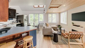 Una cocina moderna con una isla central, un comedor con sofá y sillones, y una sala de estar con televisor y chimenea.