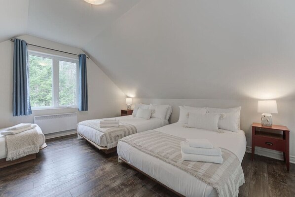 Un dormitorio con dos camas, una ventana con cortinas, una mesita de noche con lámpara y un calentador bajo la ventana.